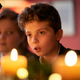A small boy looks aghast while sitting at a festive dinner table decorated with candles.